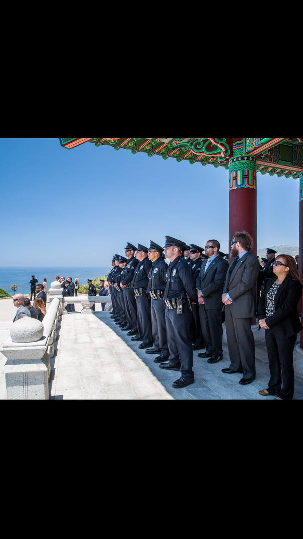 A row of uniformed officers and civilians standing in a line under a pavilion, facing the ocean.