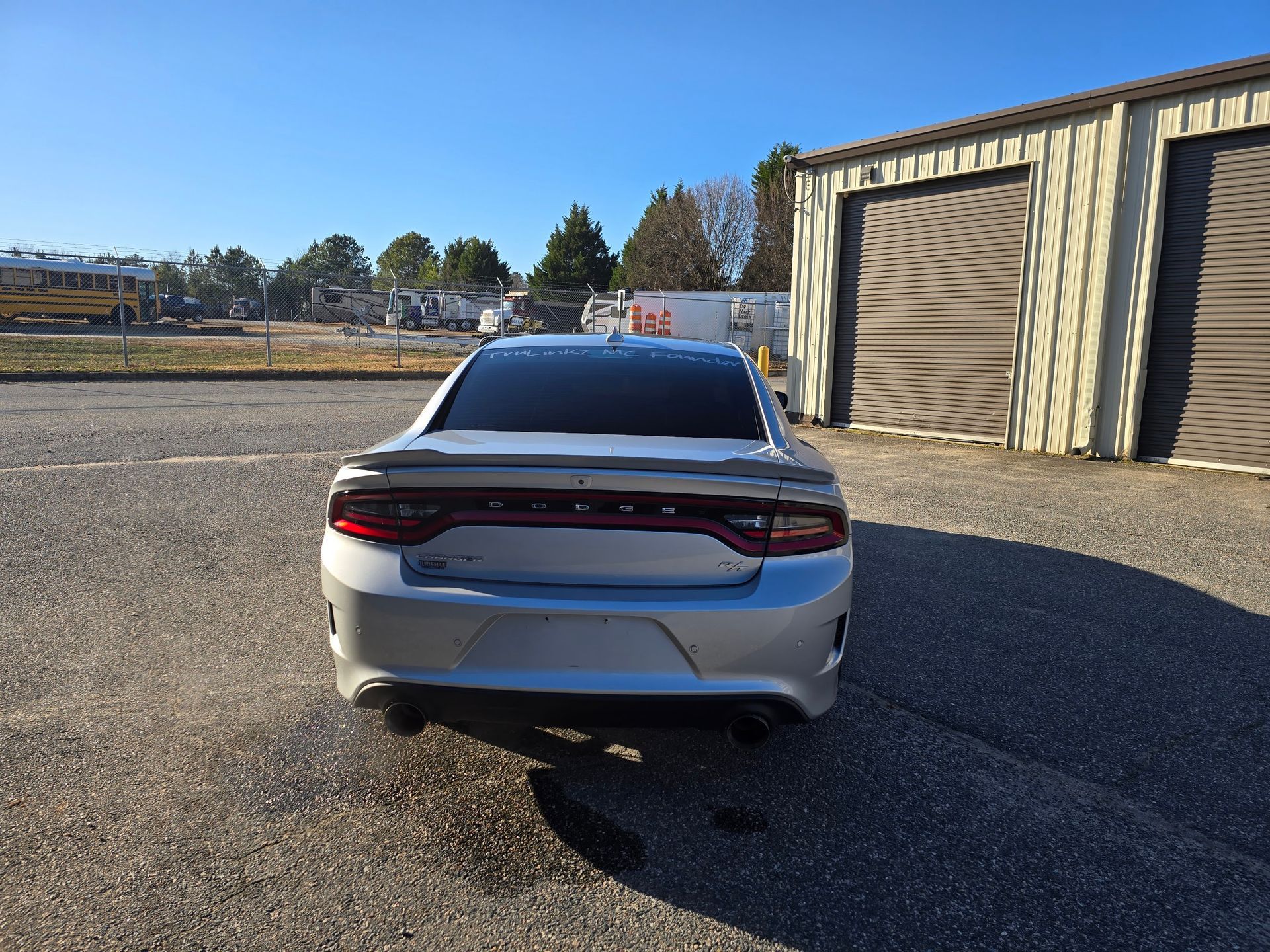 A silver Dodge Charger parked on a gravel lot in front of a tan metal building under a clear blue sky.