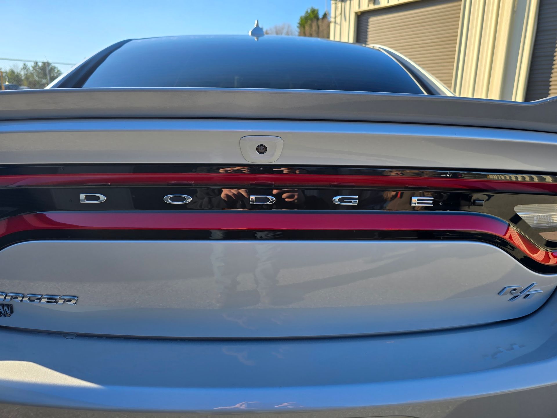 Close-up of the rear trunk of a silver Dodge Charger, showing the red LED taillight bar, Dodge lettering, and an R/T badge.