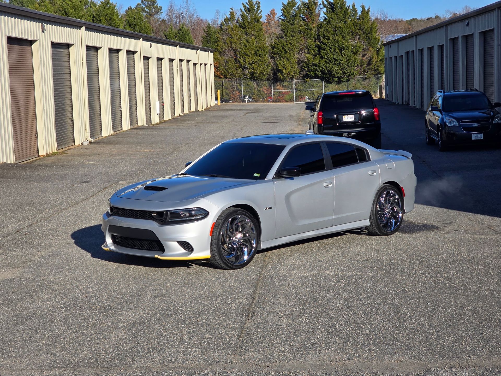 A silver Dodge Charger parked in an outdoor storage facility lot with two other cars visible in the background.