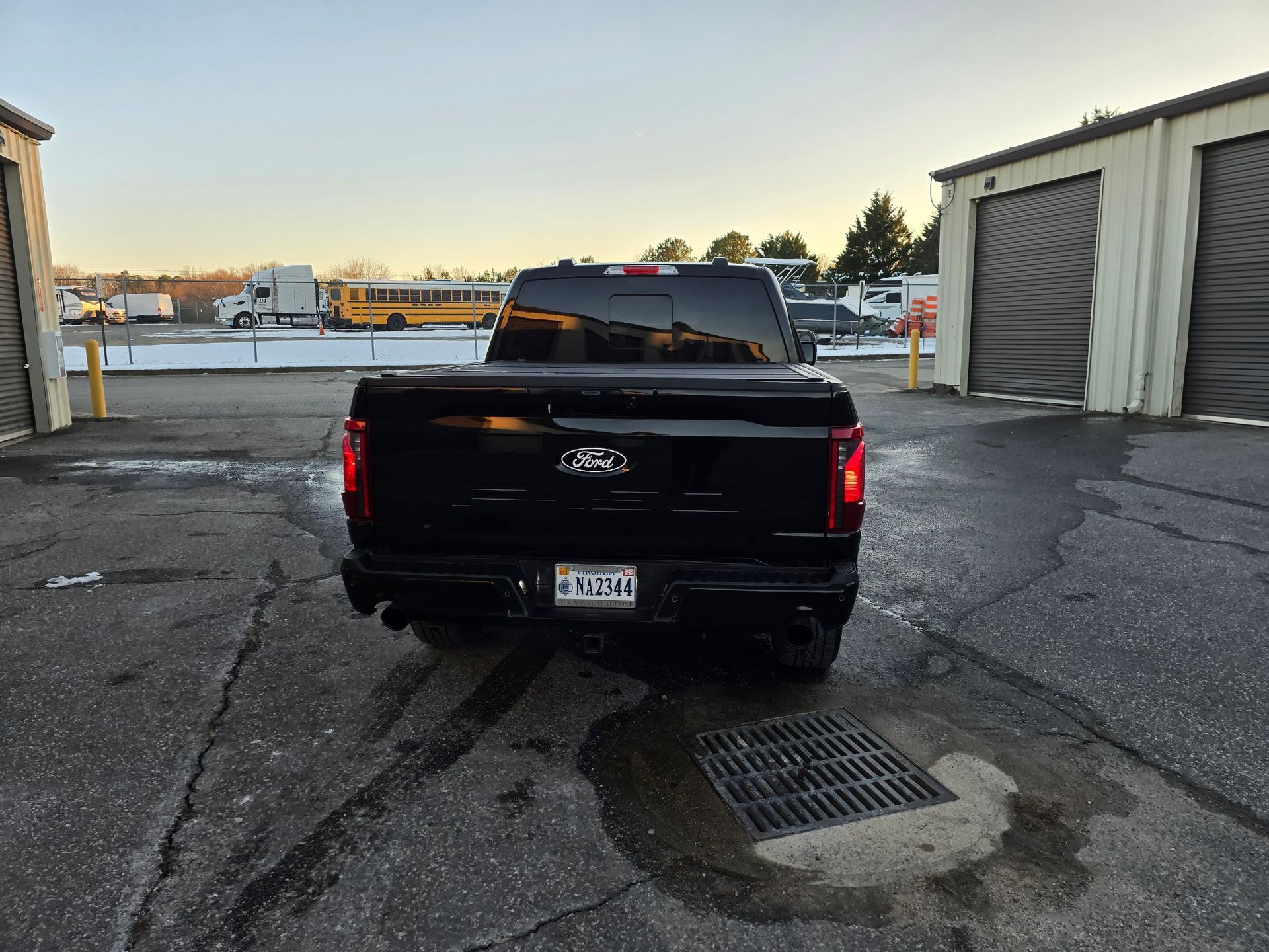 A black Ford pickup truck parked in an outdoor lot on a sunny day with a school bus visible in the background.