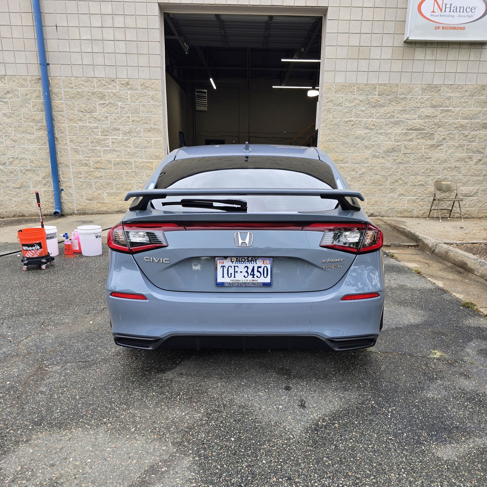 Rear view of a gray Honda Civic with a rear spoiler, parked outside a garage.