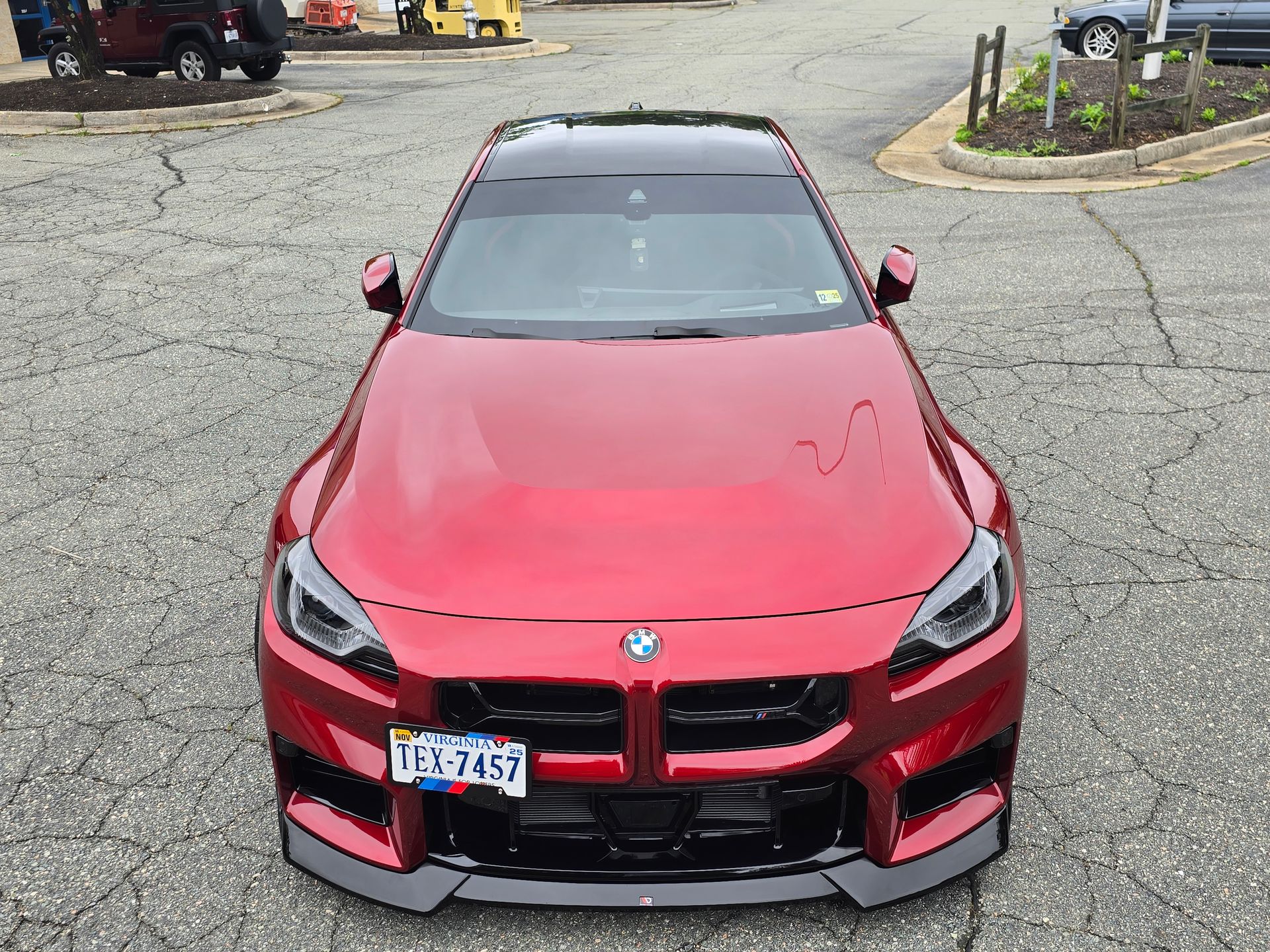 A red BMW M2 parked on asphalt, featuring a black roof, front splitter, and a license plate, viewed from the front.
