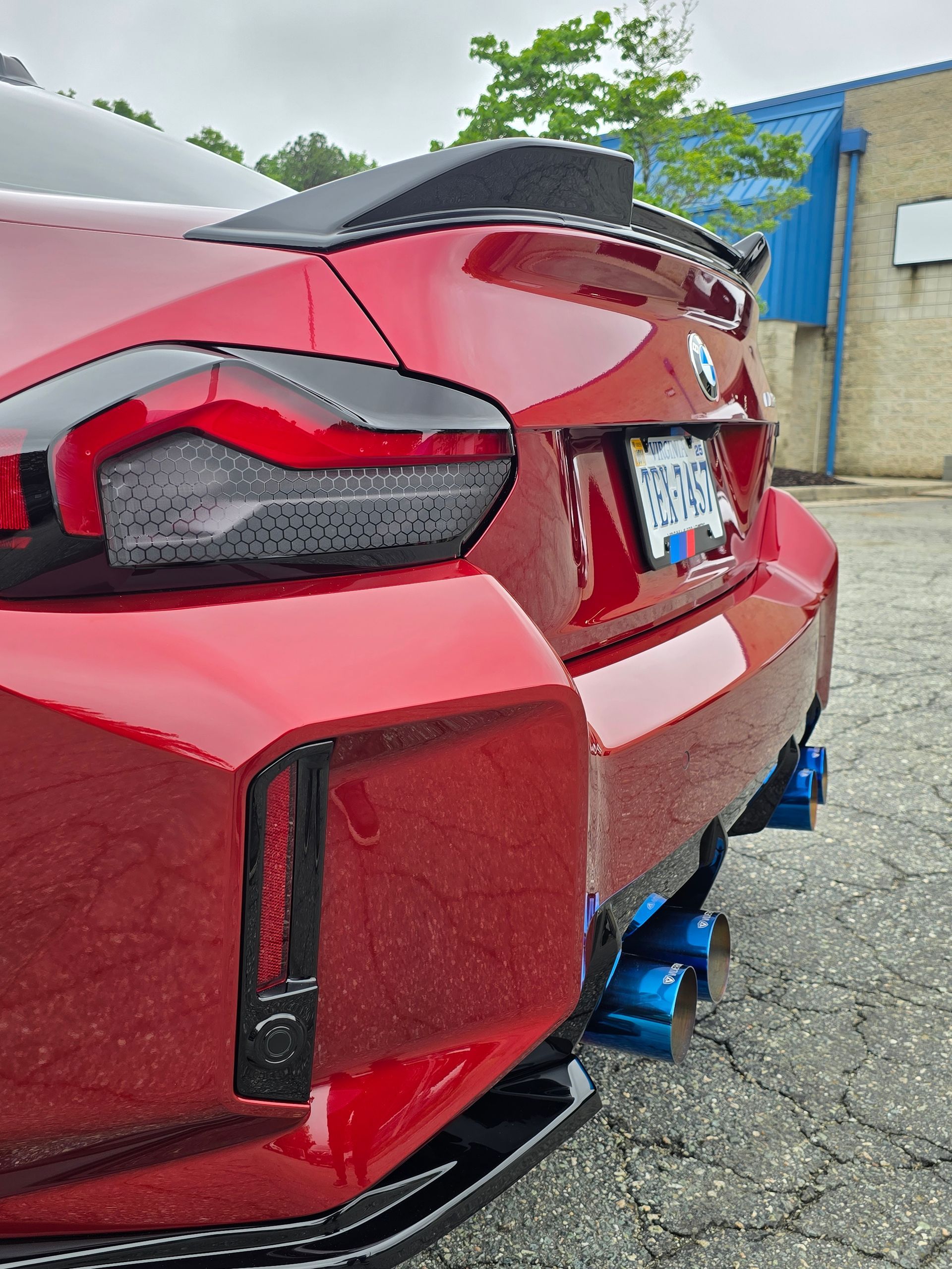 Close-up, low-angle view of a red car’s rear, featuring a black spoiler, tinted taillights, and blue exhaust tips.