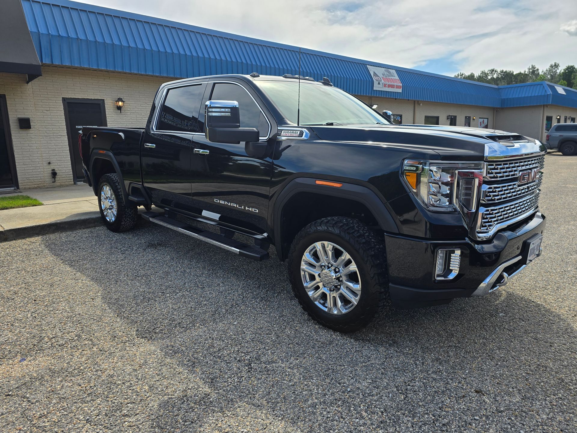 Black GMC Sierra truck parked in front of a blue-roofed building on a gravel surface.
