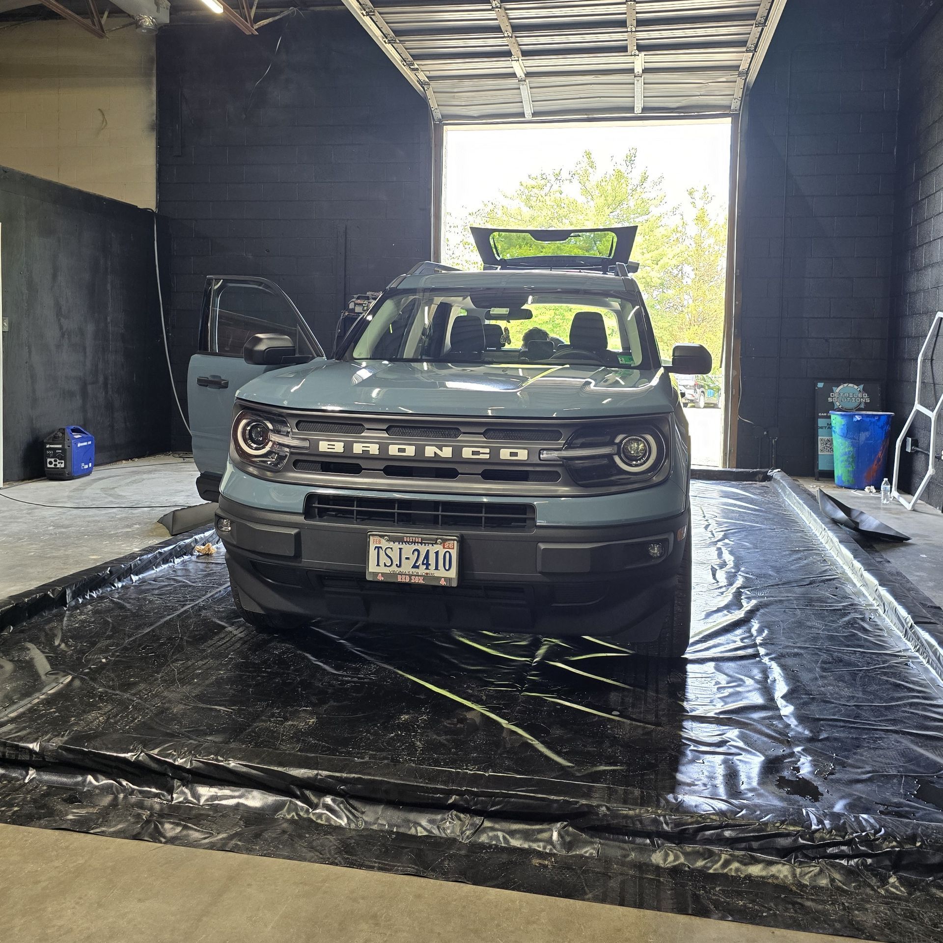 Blue Ford Bronco in a car wash, door open, on a black mat.