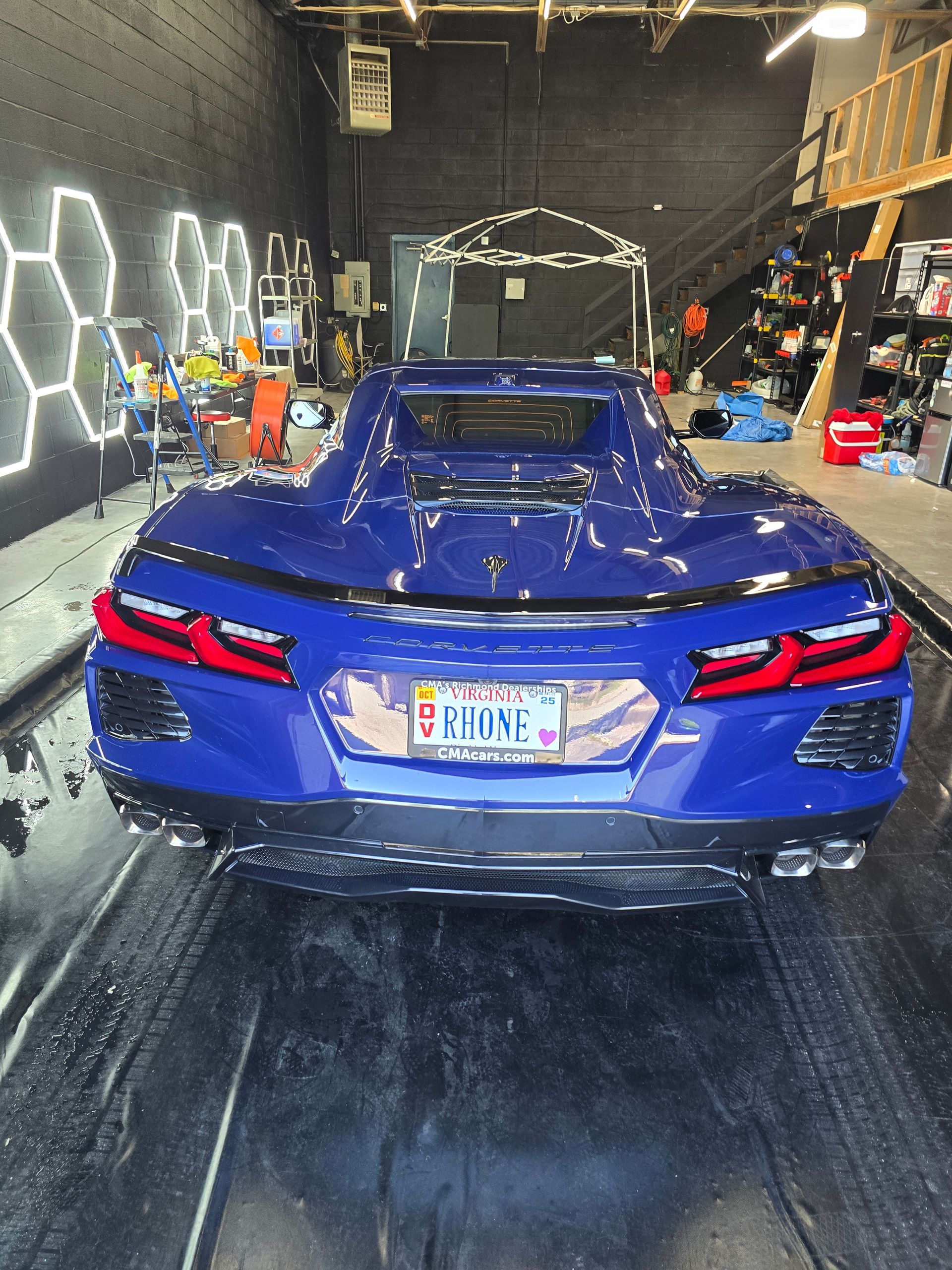 Blue Chevrolet Corvette in a car wash bay, rear view, license plate visible.