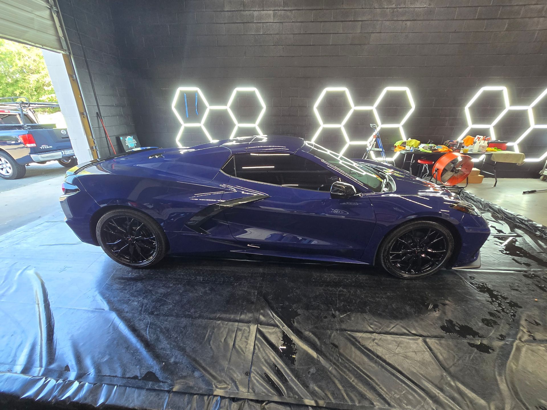 Blue sports car inside a garage with honeycomb lights. Car is parked on a wet surface.