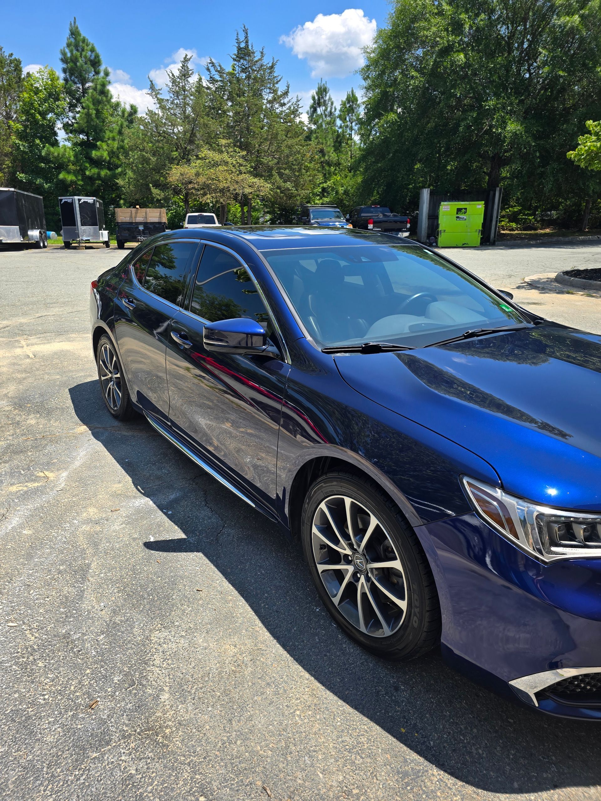 Blue sedan parked on asphalt, sunny day. Dark tinted windows and alloy wheels.
