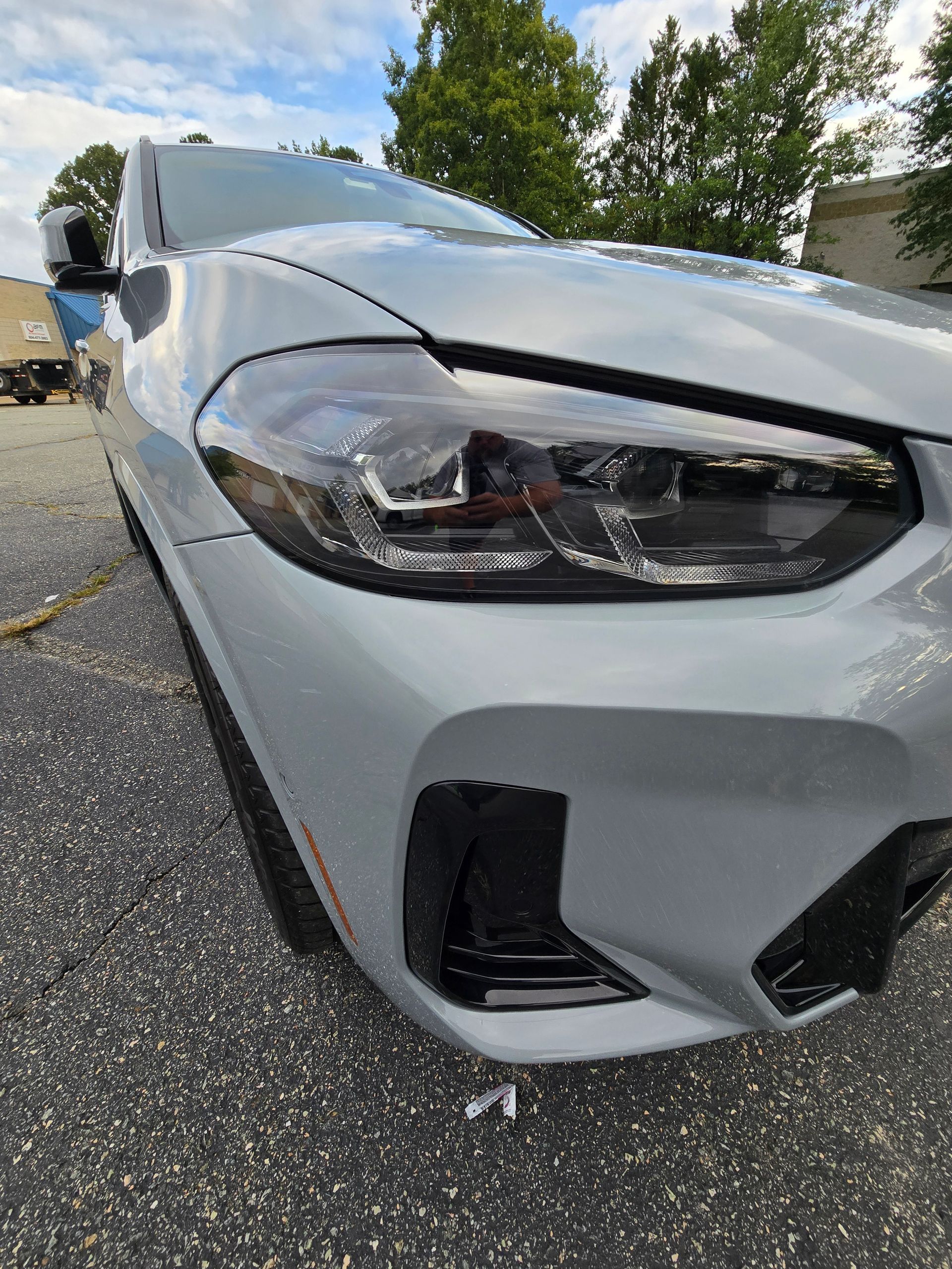 Gray BMW car headlight and front bumper, angled view outdoors.