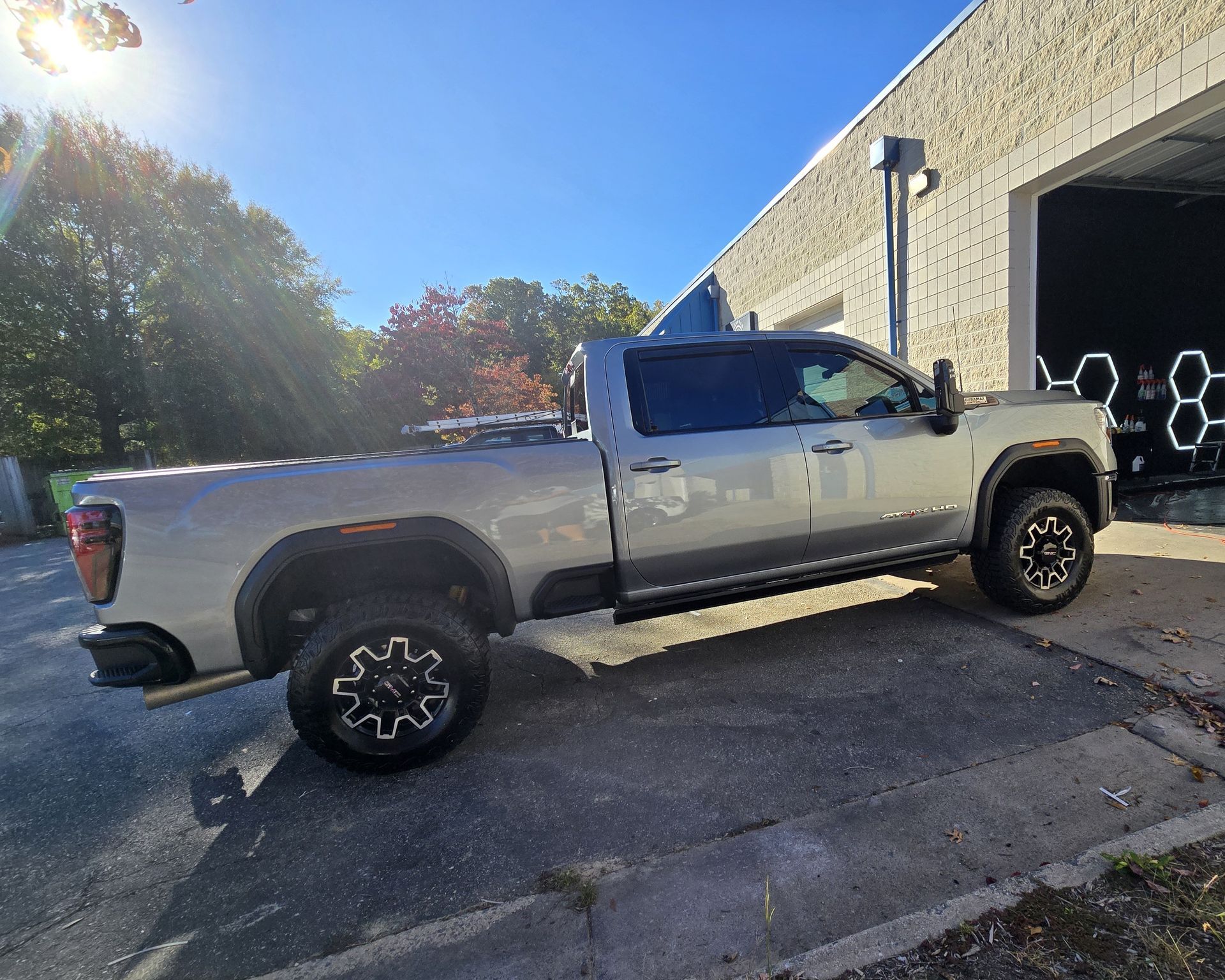 Silver pickup truck parked next to a building, with black rims and a blue sky.