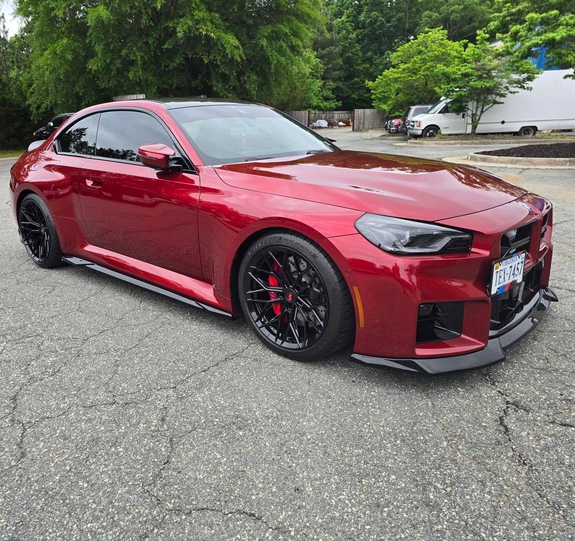 Red sports coupe with black wheels parked on a tree-lined street