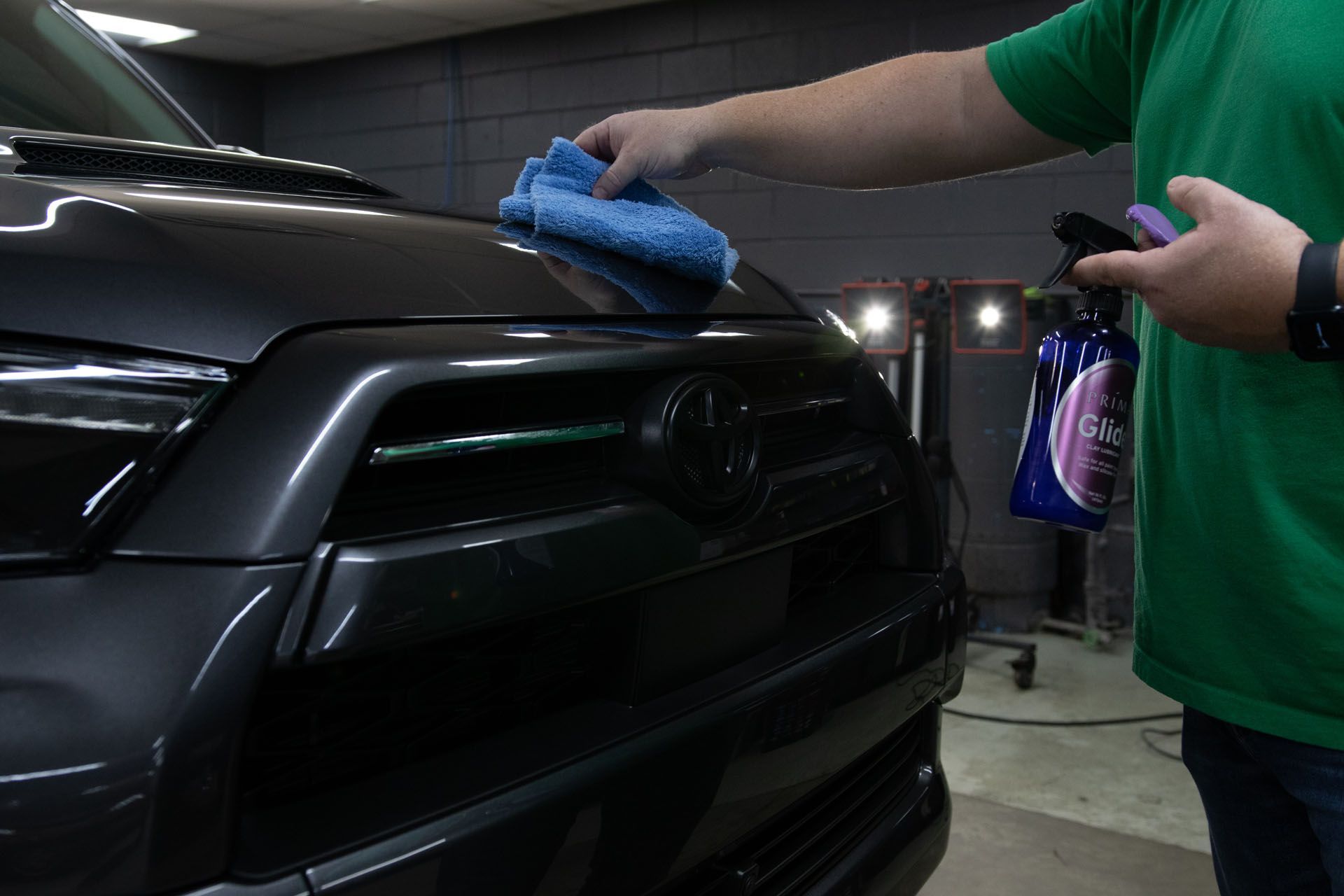 A man in a green shirt is cleaning the hood of a car with a towel .