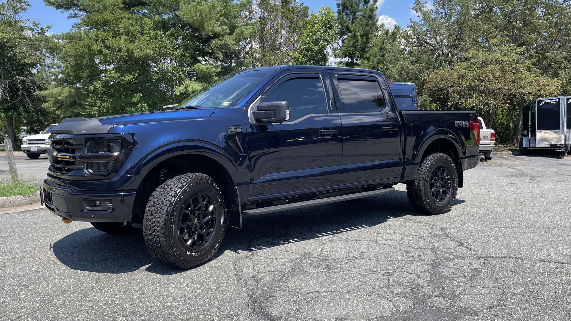 Dark blue Ford F-150 truck with black wheels parked in a lot, sunny day.