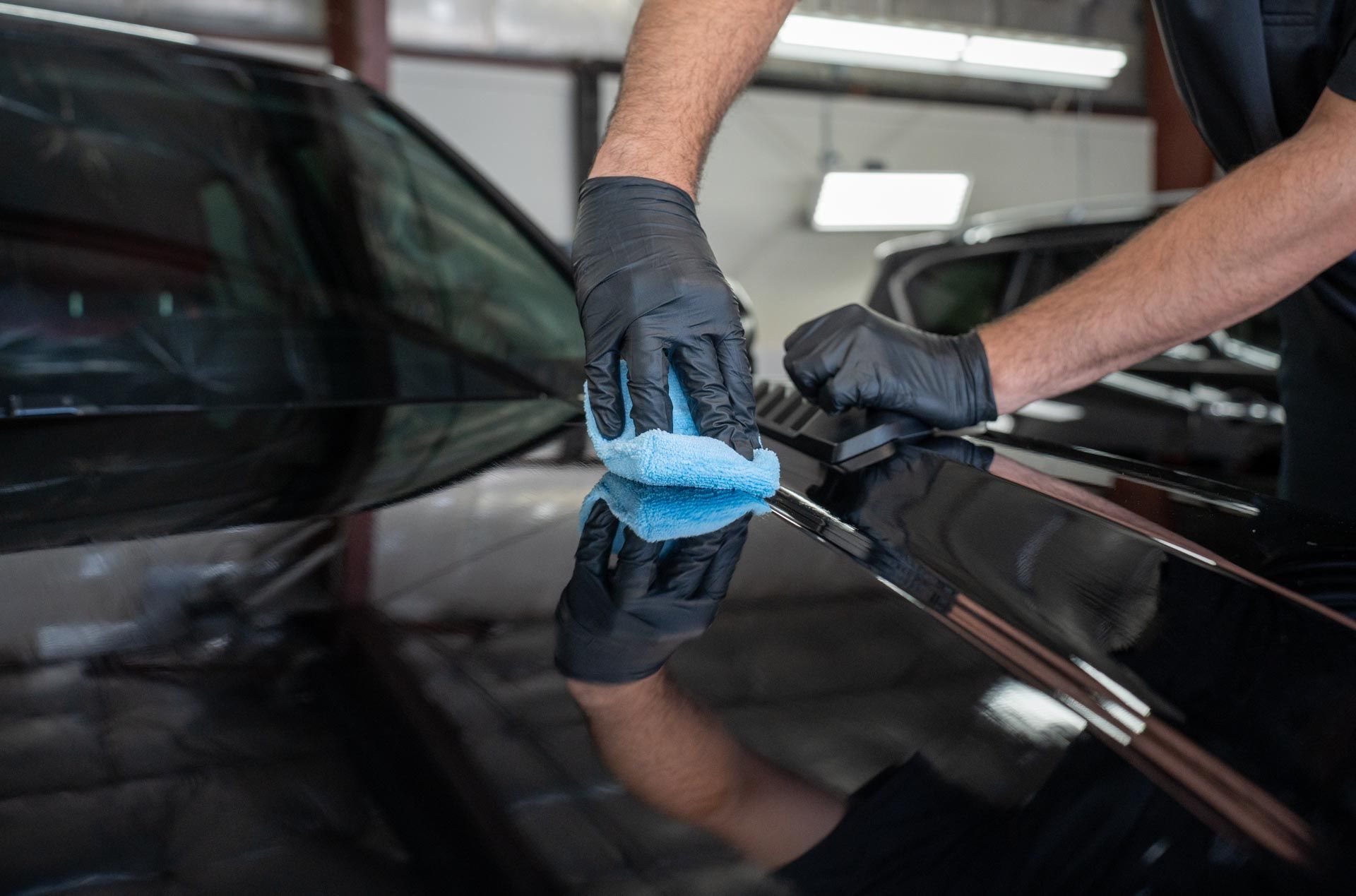 Technician applying ceramic coating to a black car hood.