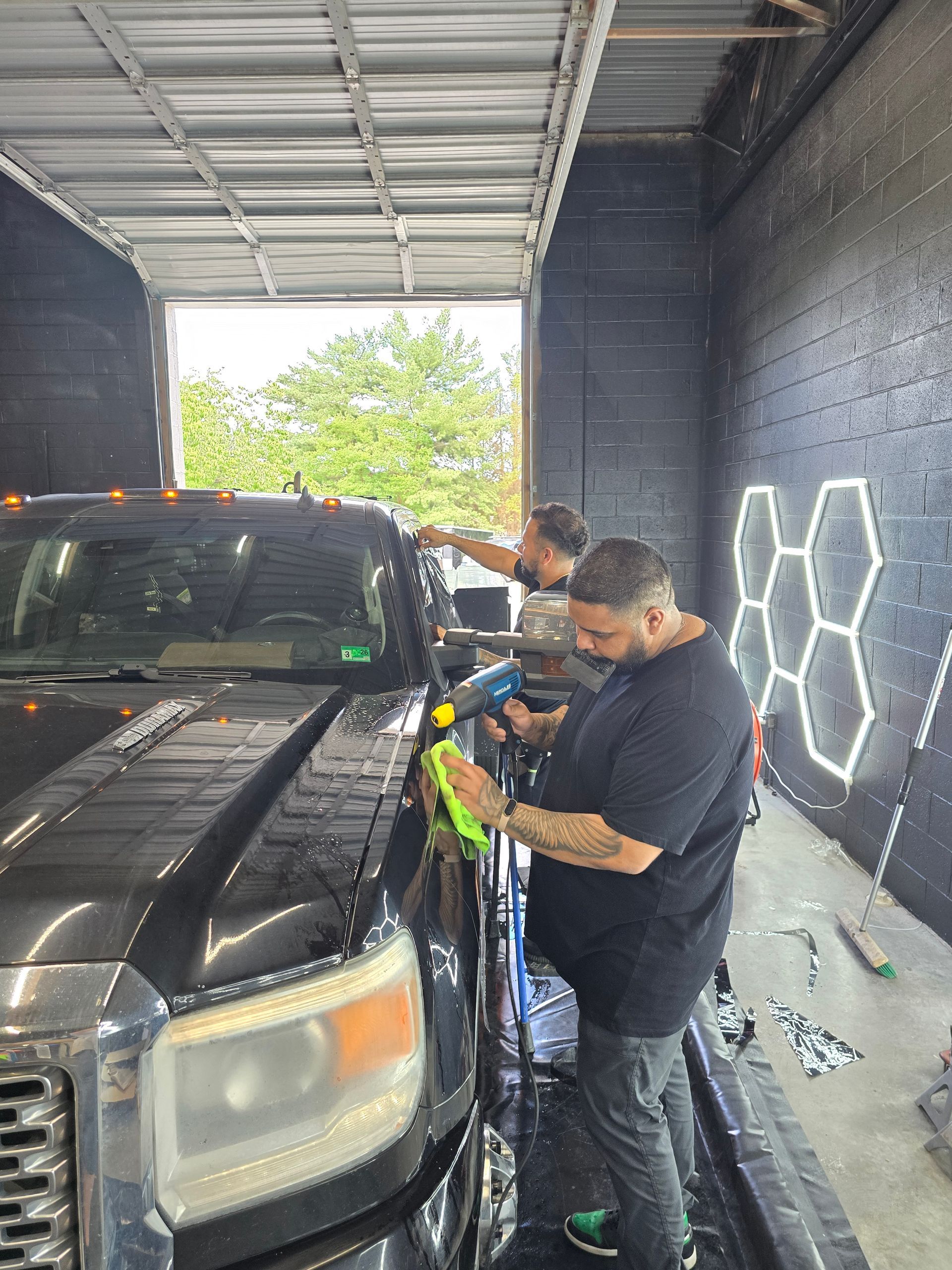 Two men applying film to a black truck's side panels. They are inside a bay, working near a decorative wall.