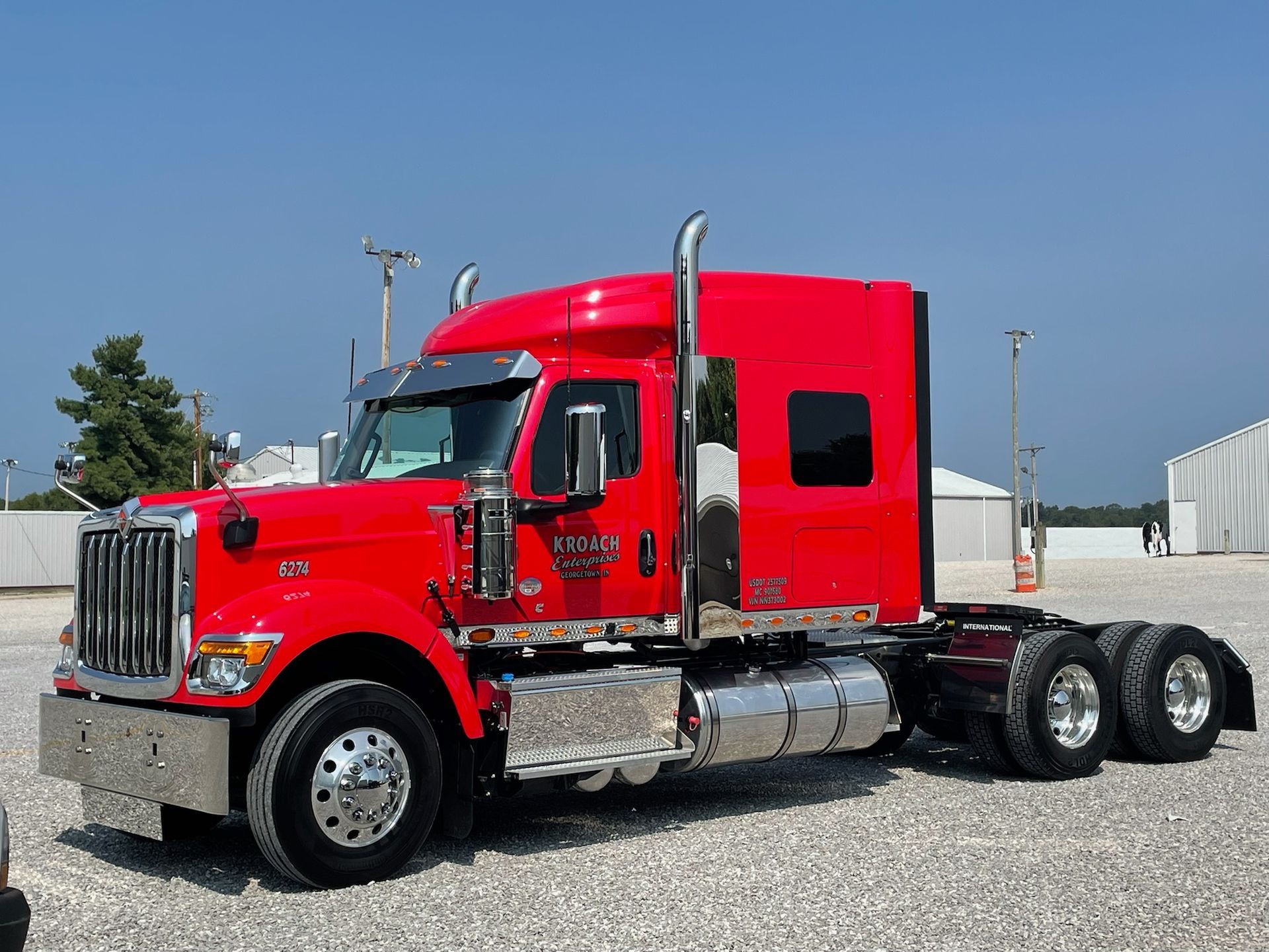 A red semi truck is parked in a gravel lot .