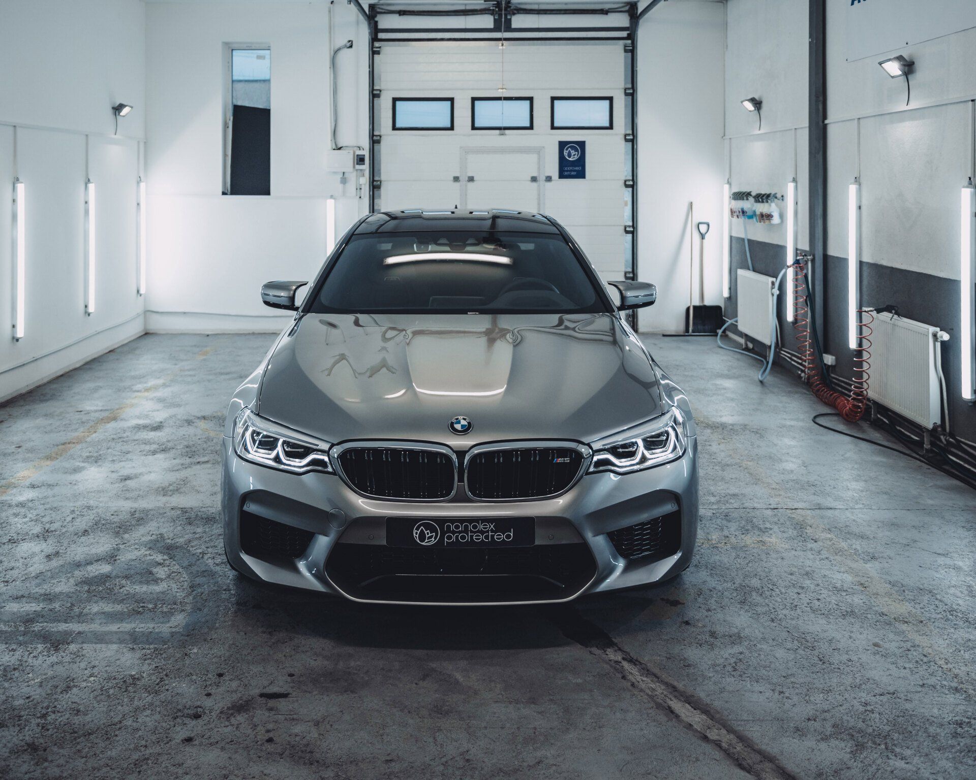 Silver BMW sedan parked in a white auto garage with concrete floor and closed overhead door