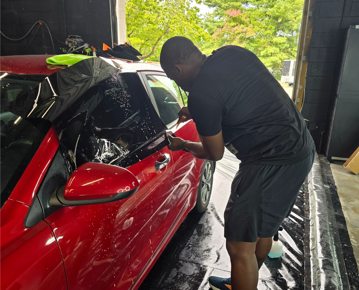 Man applying tint to a red car window in a garage.