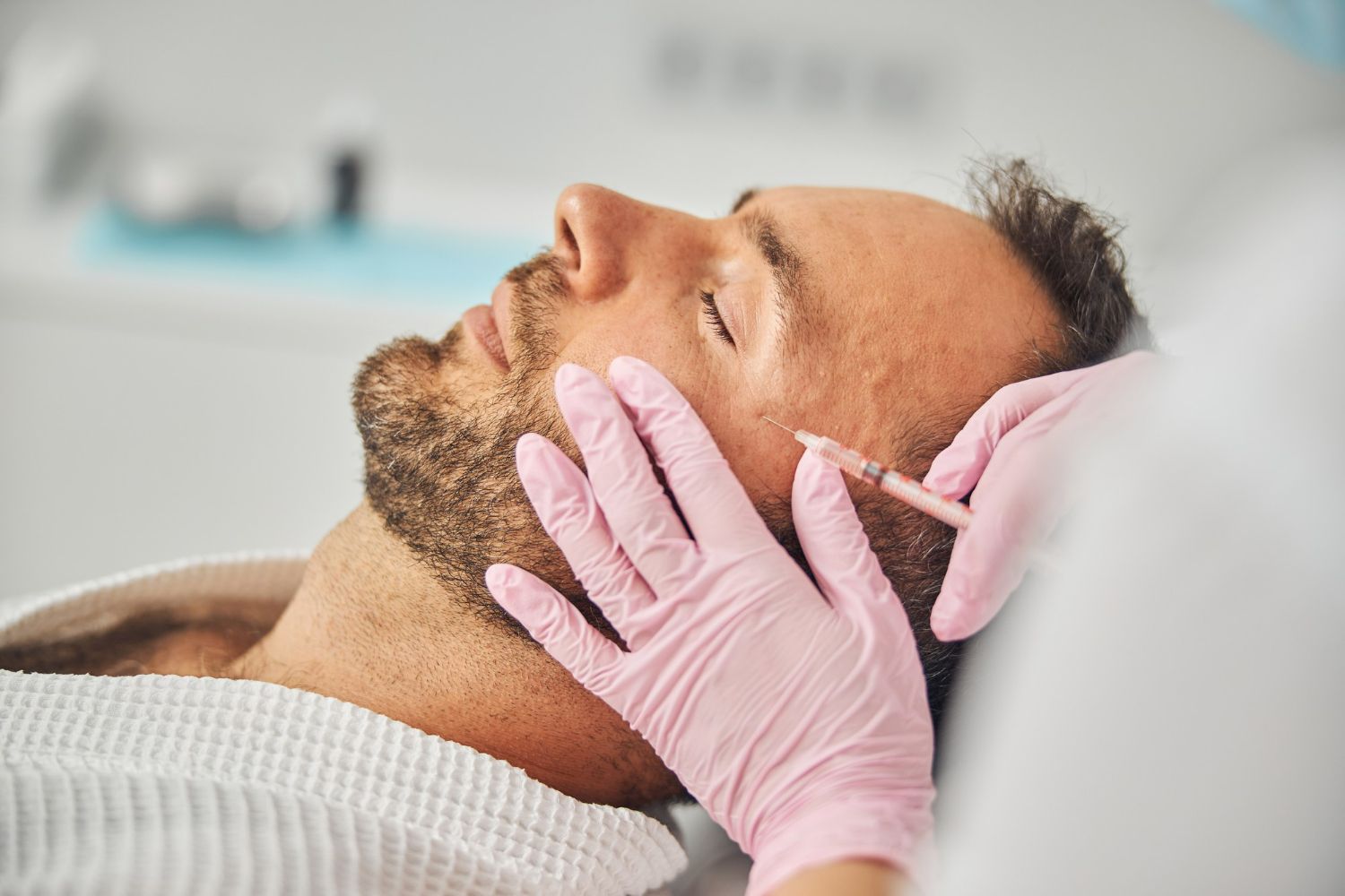 A medical professional in pink gloves performs a facial injection on a person lying down in a clinic setting.