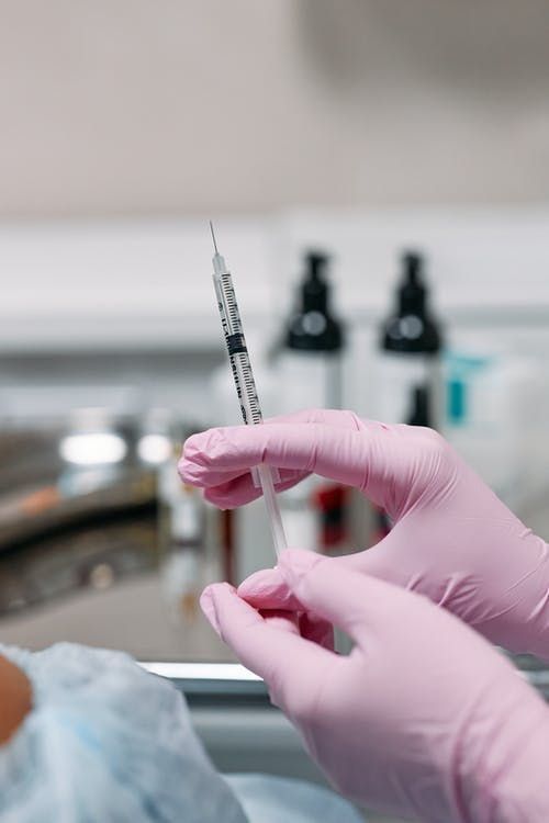 A person wearing pink gloves is holding a syringe in their hand.