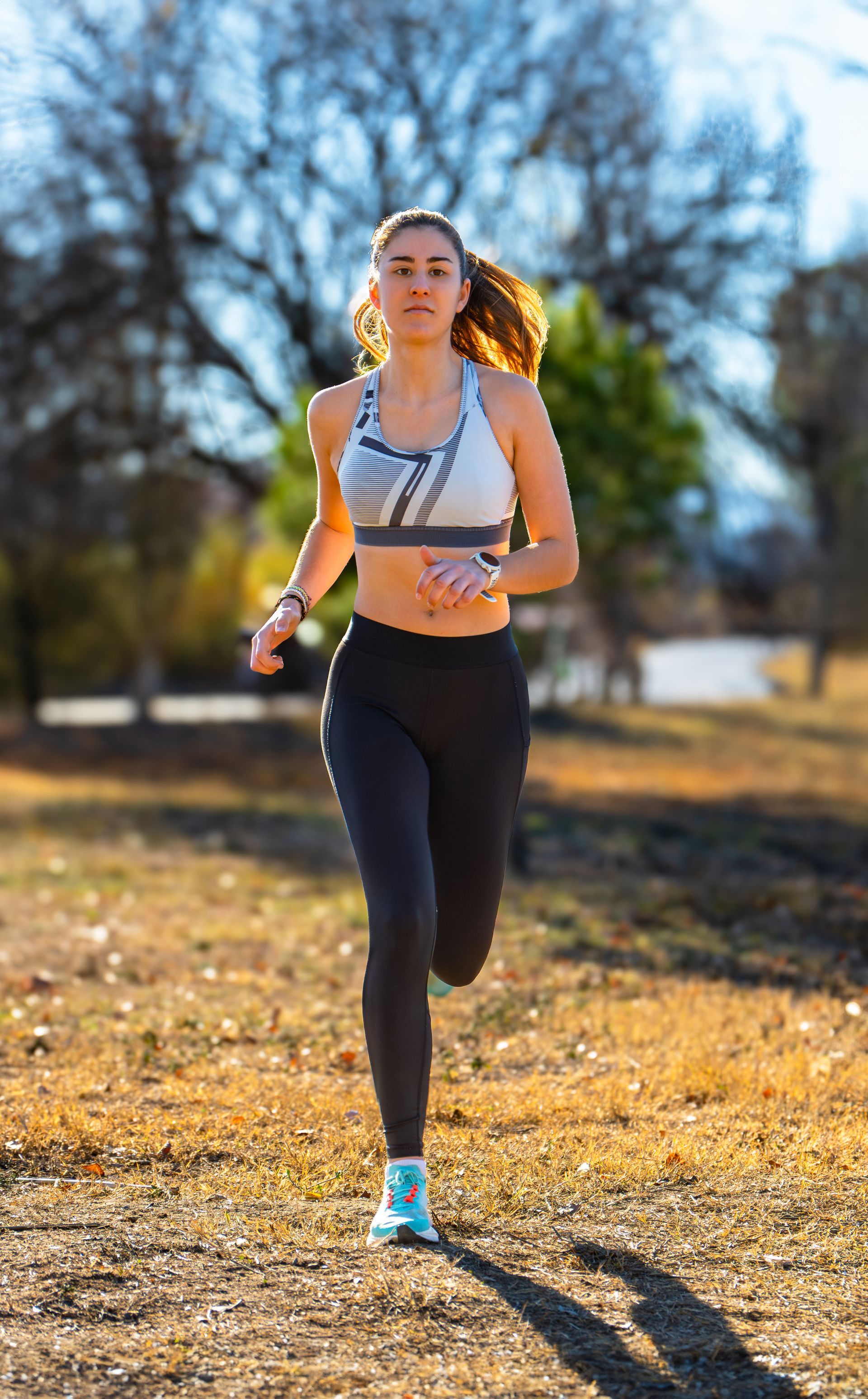 A woman in a sports bra and leggings is running in a park.