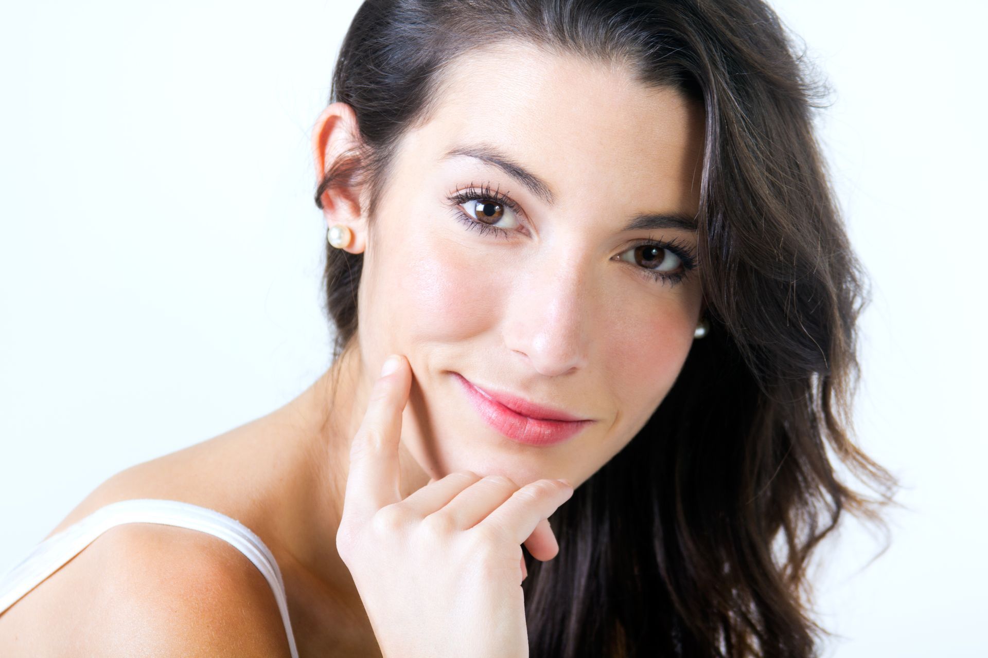 Close-up of a woman with dark hair, resting her chin on her hand and smiling softly against a white background