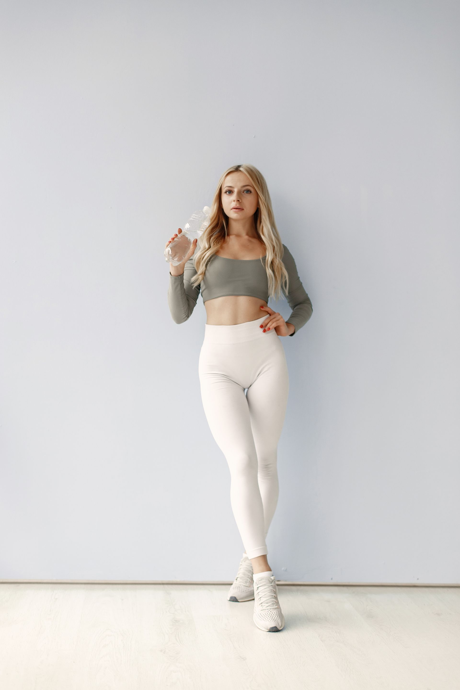 A woman in a crop top and white leggings is standing in front of a blue wall.