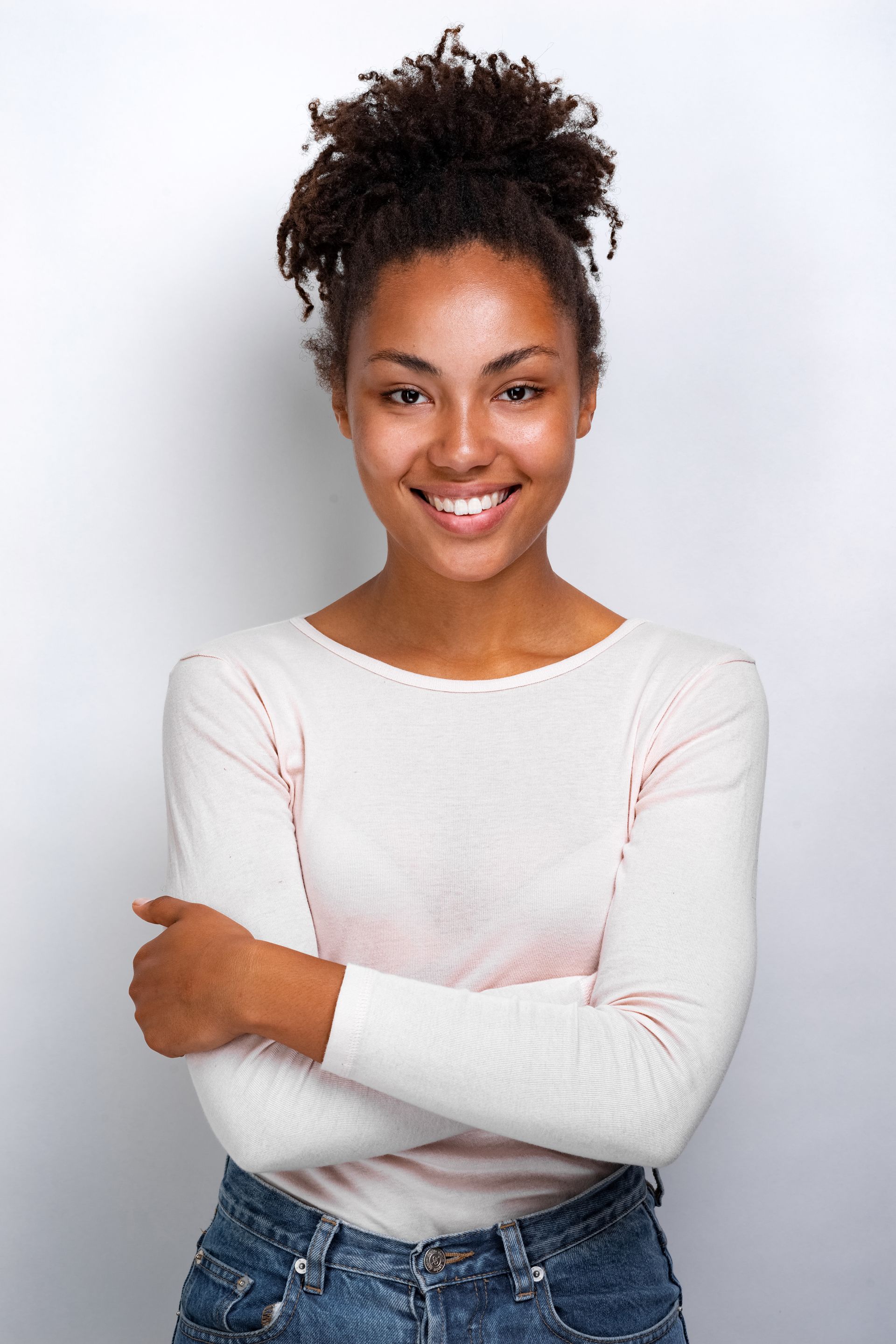 A young woman is standing with her arms crossed and smiling.
