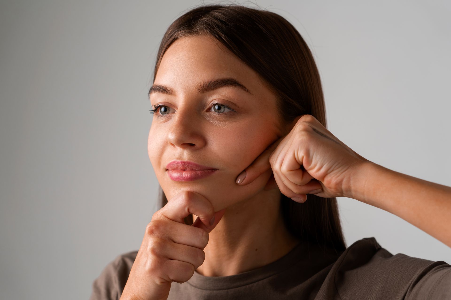 Person demonstrating facial massage with both hands against a light gray background