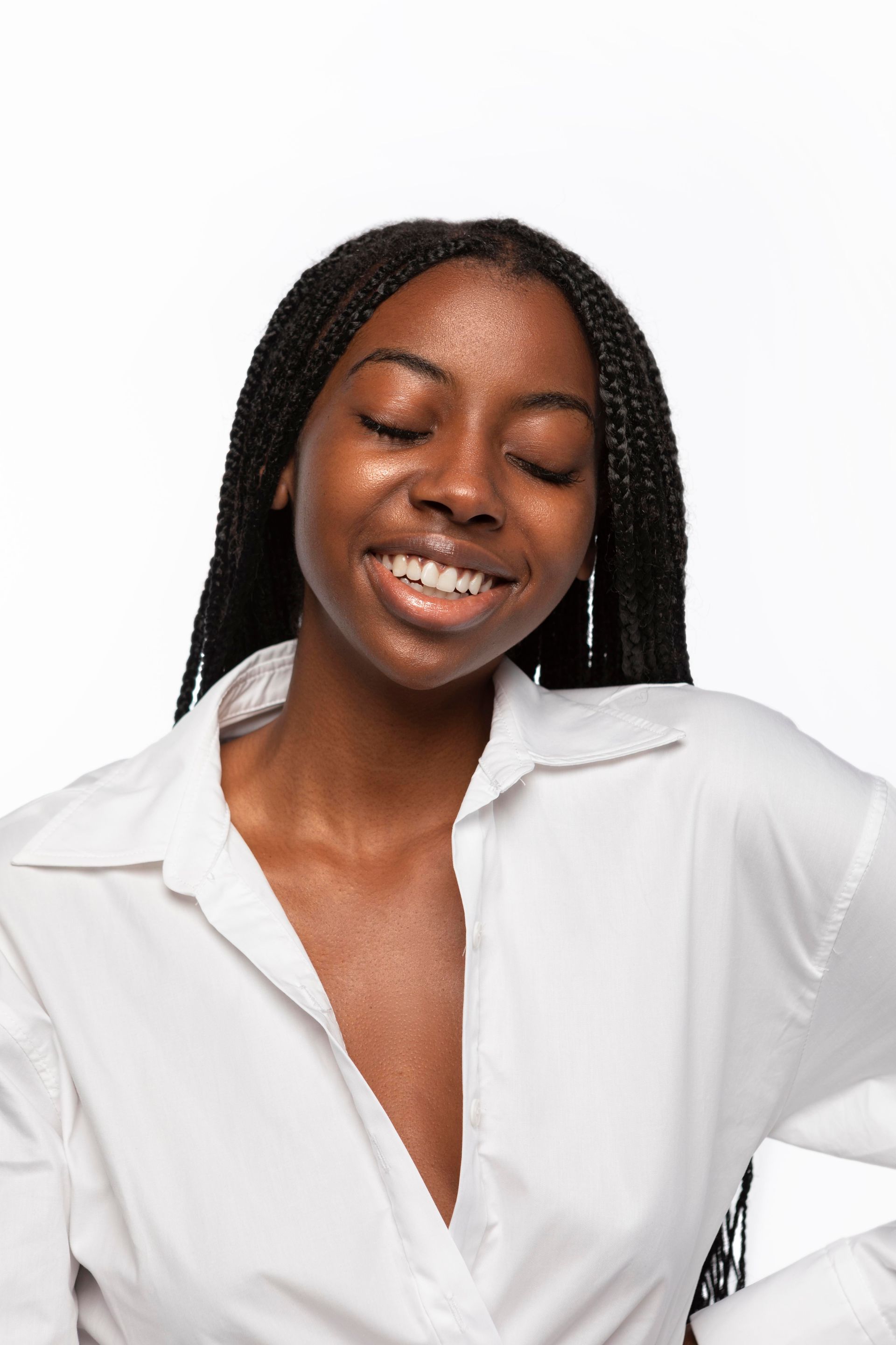 A woman with braids is wearing a white shirt and smiling.