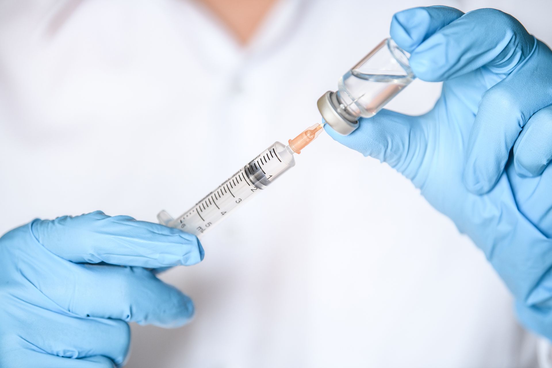 Gloved hands drawing vaccine from a vial into a syringe
