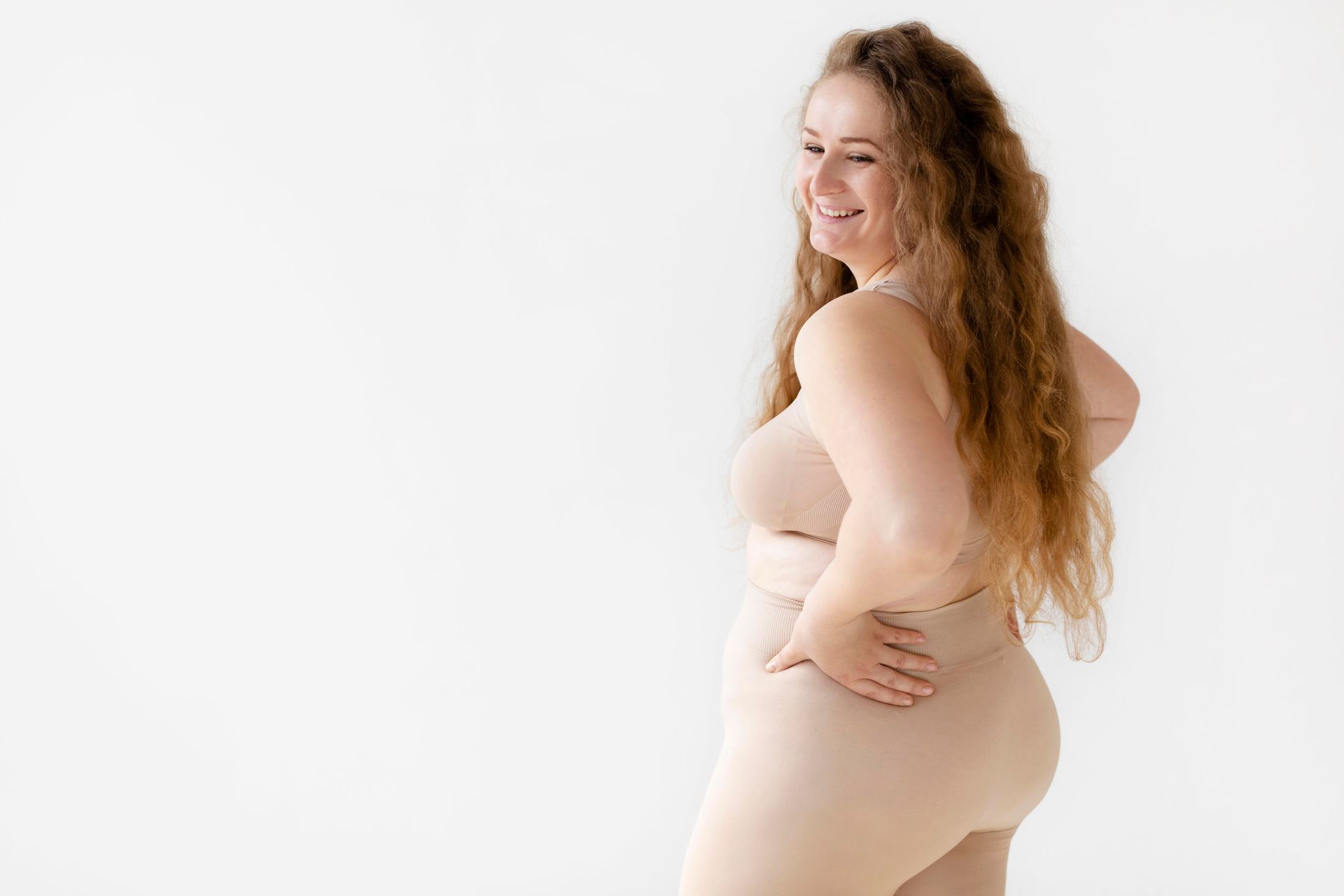 A plus size woman is standing with her hands on her hips and smiling.
