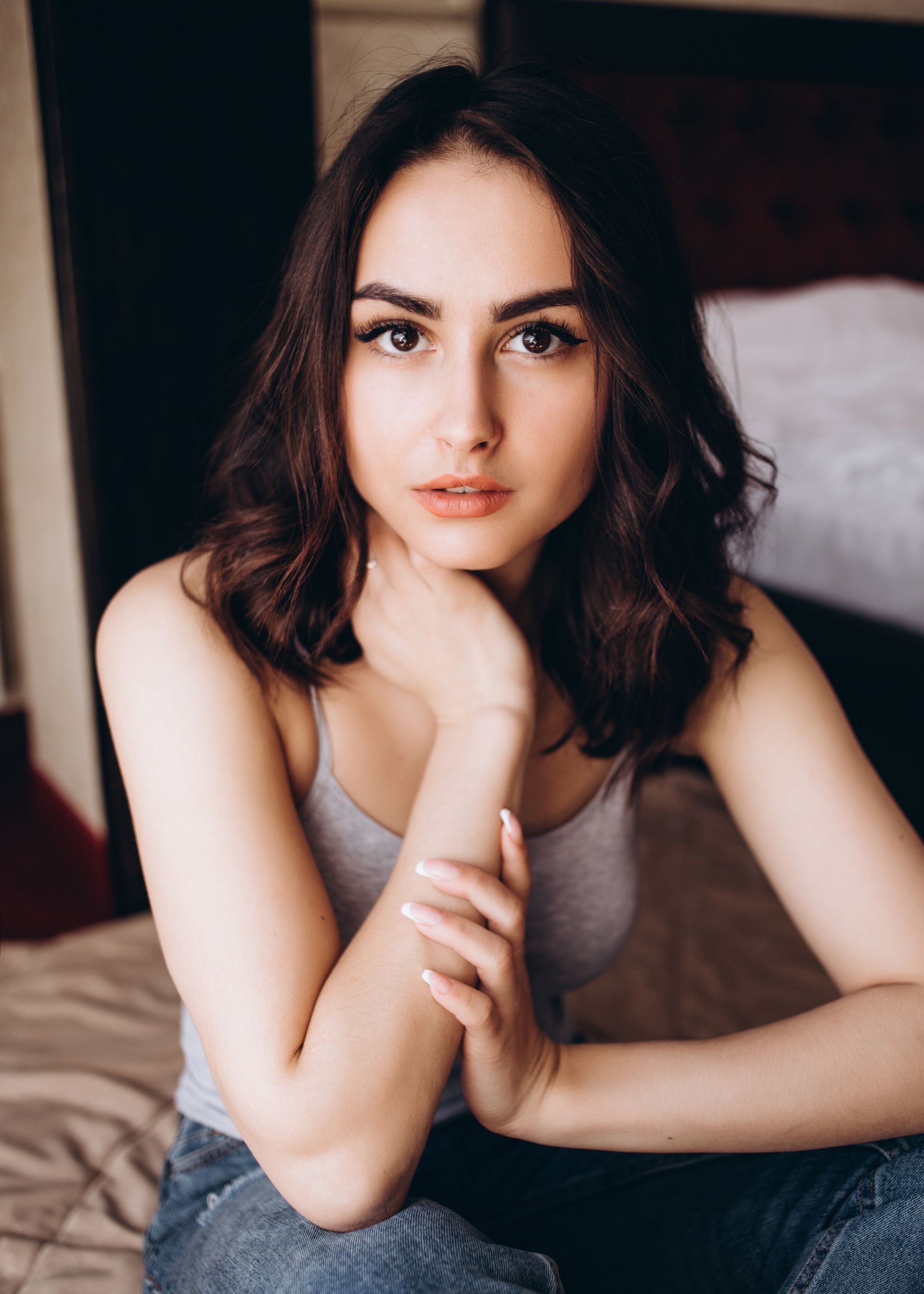 A woman is sitting on a bed with her hand on her chin.
