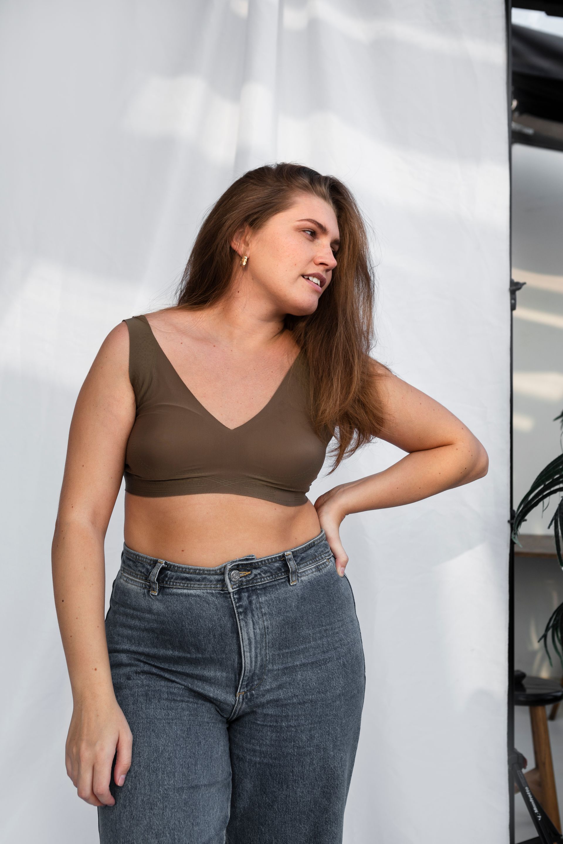 A woman in a crop top and jeans is standing in front of a white wall.