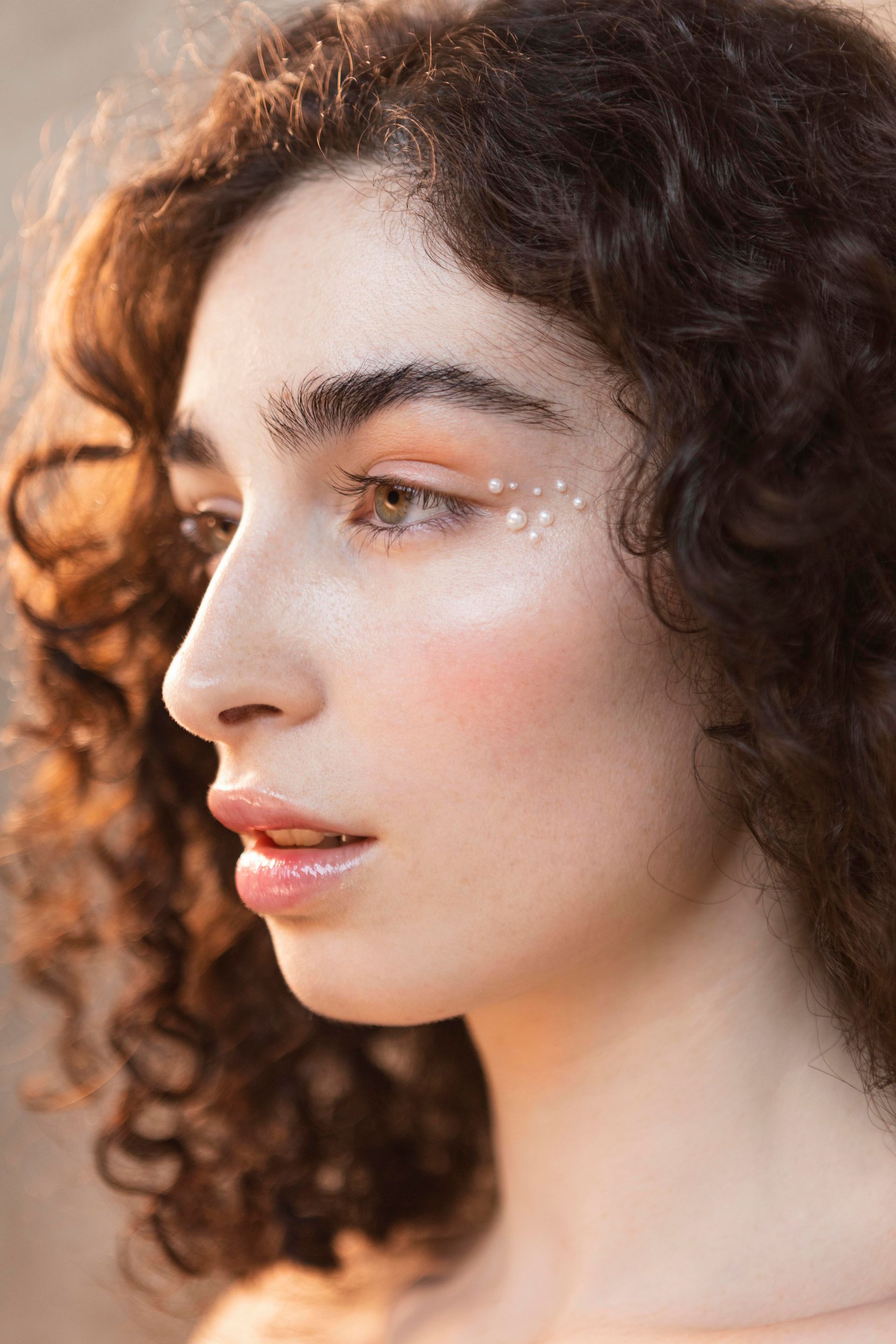 A close up of a woman 's face with curly hair and pearls on her eyes.
