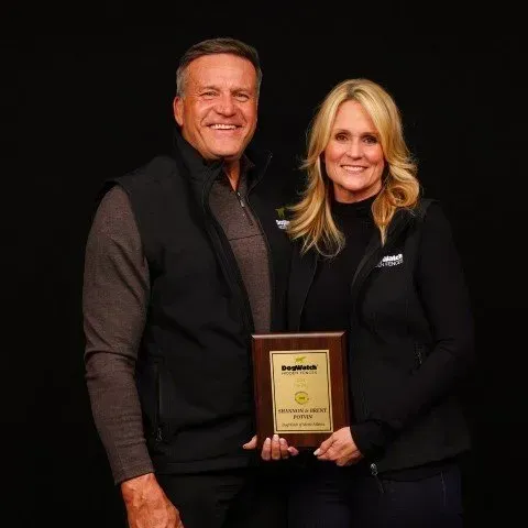 Couple holding award in front of a black backdrop; smiling.