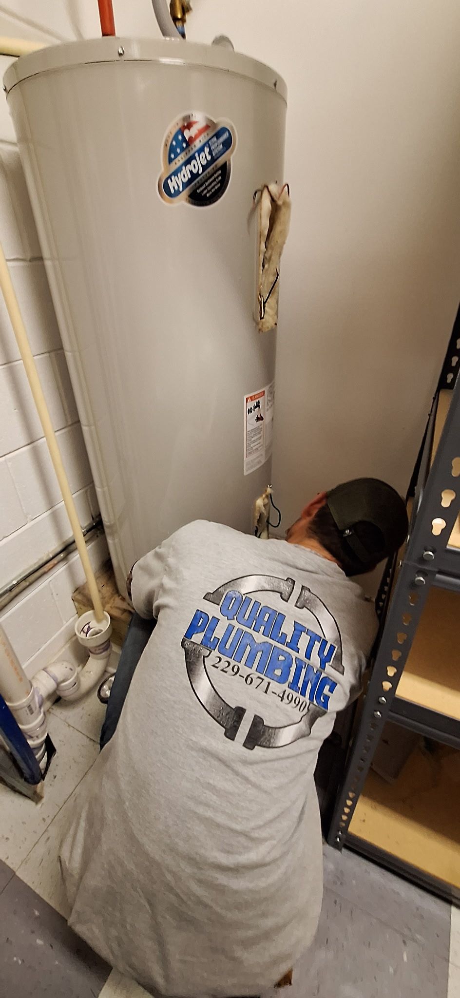 Technician in blue coveralls fixing a white wall-mounted boiler, using tools and standing on a small step ladder.