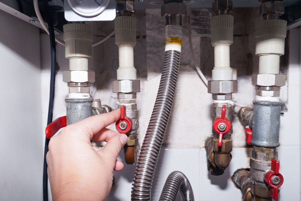 Hand turning a red valve on a water heater, close-up view.