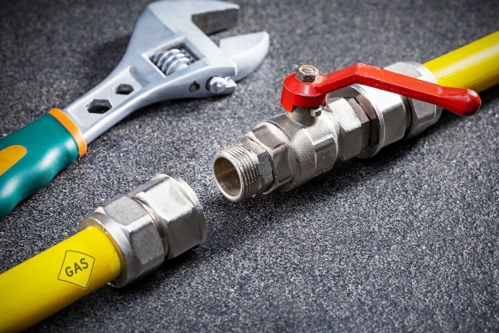 Wrench and gas line fitting with a red valve, for plumbing repairs. Yellow gas line.