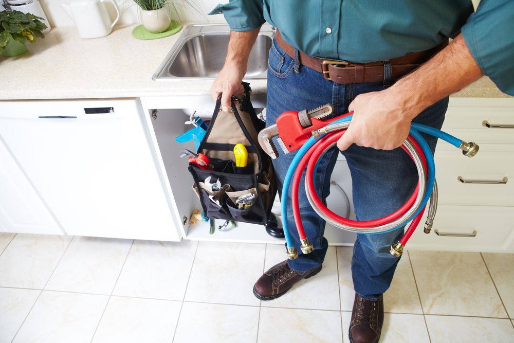 Plumber with tools and hoses near a kitchen sink.