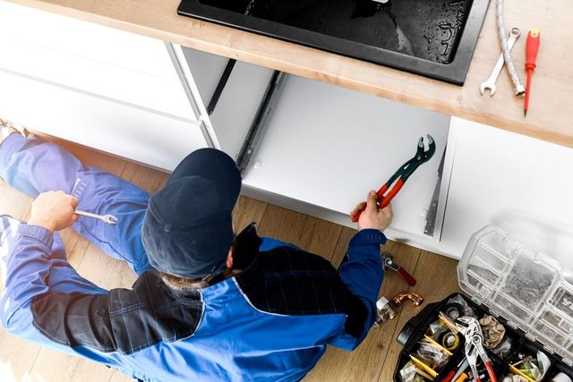 Plumber installing water pipes in a confined space; using tools to connect white pipes.