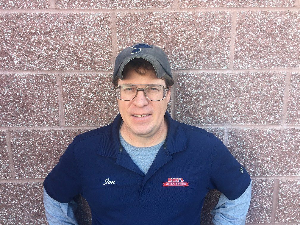 Man in a navy shirt and cap standing against a brick wall, smiling at the camera.