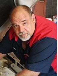 Man in red-and-navy shirt leaning over equipment, looking at the camera.
