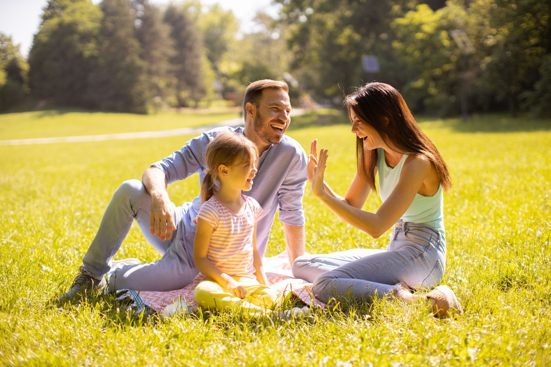 A boy is playing a guitar while sitting on the grass with his grandparents.