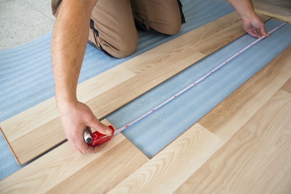 A Man Is Measuring a Piece of Wood with A Tape Measure — Lismore Floor Sanding in Mullumbimby, NSW