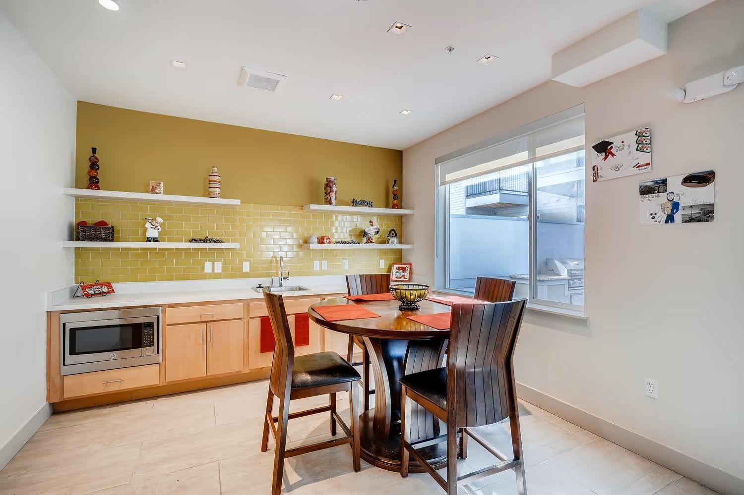 A kitchenette with light wood cabinets, yellow tile, open shelves, and a round dining table with four chairs.