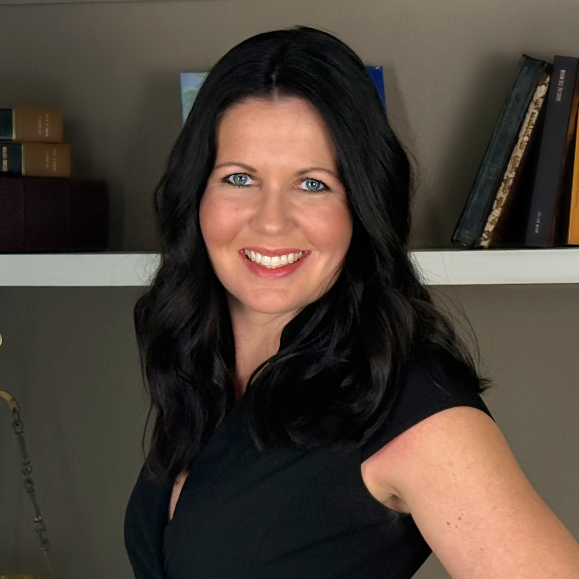 Woman smiling with arms crossed, wearing a black top against a white wall.