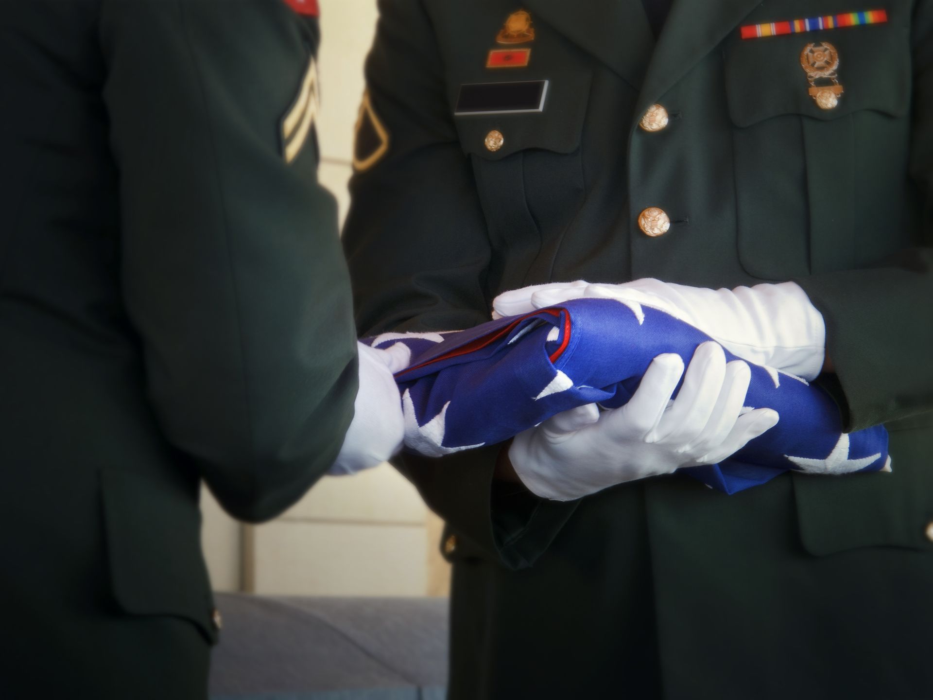 Two soldiers in green dress uniforms and white gloves formally folding an American flag.