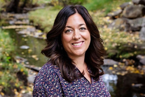 Smiling woman in a floral blouse outdoors by a rocky stream and greenery